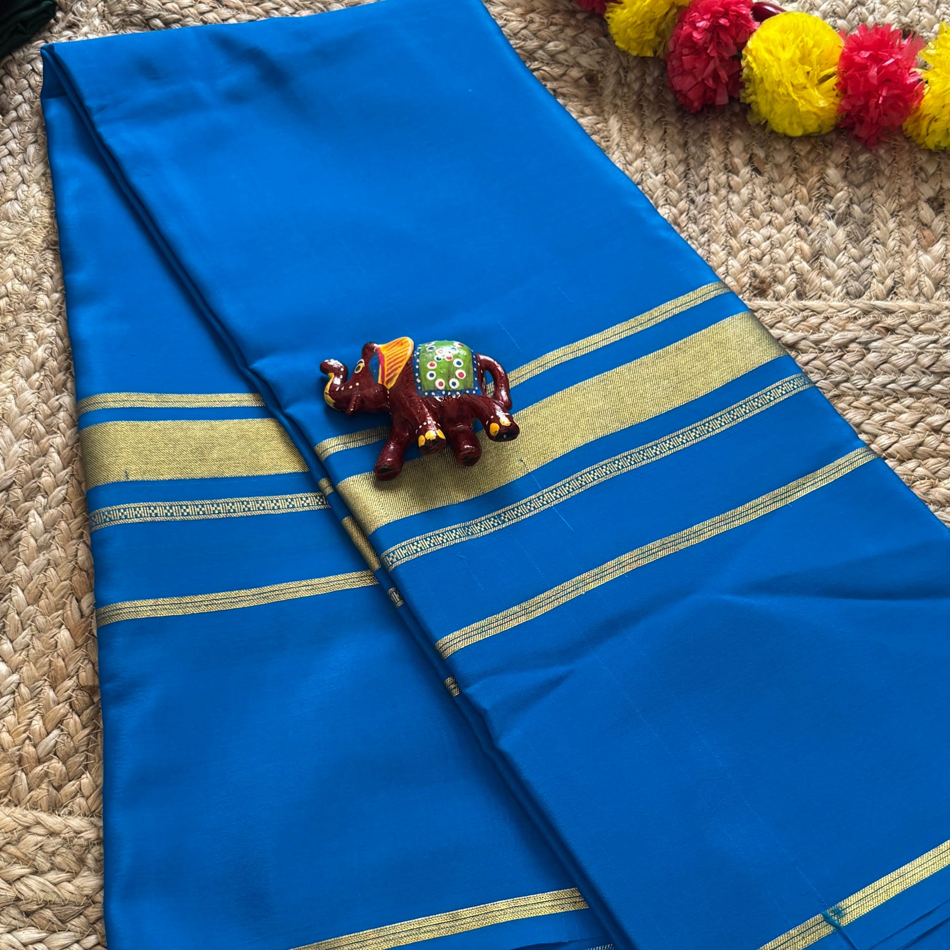 Blue saree with gold border on a textured surface with decorative items.